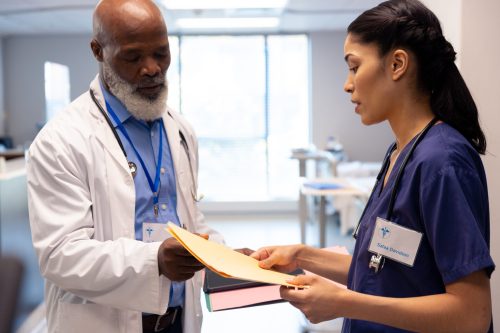 Diverse female and senior male doctor looking at file, talking in hospital ward, copy space. Hospital, medical and healthcare services.